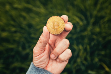 Farmer holding Bitcoin cryptocurrency coin in green barley field, selective focus