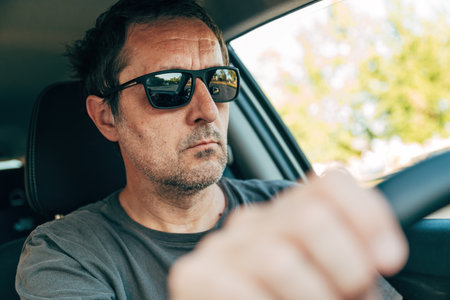 Cool mature adult male driver with black sunglasses driving a car along the road, selective focus