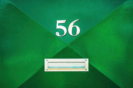 House number 56 on green metal door and mailbox slot. Fifty six in worn metallic numerals. Copy space included.の写真素材