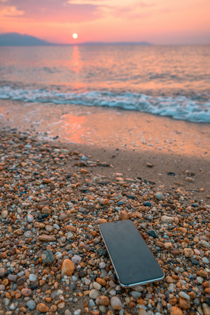 Broken discarded smartphone on the beach in summer morning, selective focus