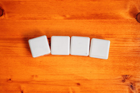 Four blank white cubes on wooden table as mockup copy space, selective focus