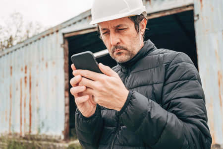 Construction engineer using smartphone at building demolition site, selective focus