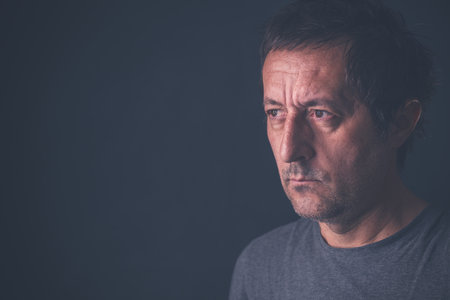 Portrait of casual serious mid-adult male wearing gray shirt in dark room, selective focus