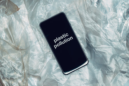 Smartphone device with Plastic pollution text on screen over polyethylene material surface, top view,の写真素材