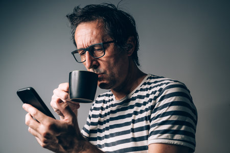Man drinking coffee and using mobile phone in dark room, selective focusの写真素材