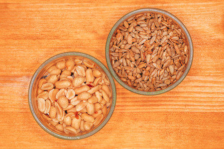 Salted peanuts and sunflower seed in glass tray on wooden table, top view