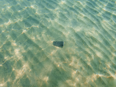Lost smartphone at the bottom of the ocean in sand, high angle viewの写真素材