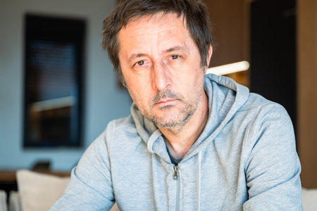 Portrait of serious casual mature adult male at home looking at camera, selective focus
