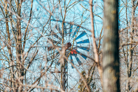 Old farm windmill turbine seen through bare tree branches, selective focusの写真素材