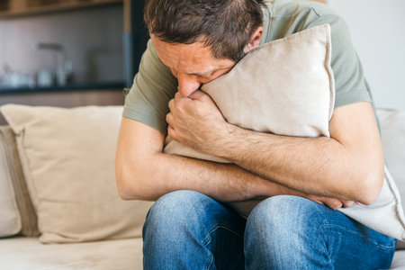 Desperate sad man sitting at sofa couch and hugging pillow, feeling miserable and depressed, selective focusの写真素材