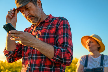 Smart farming, using smartphone app on canola rapeseed plantation field, portrait of two farmers, male and female, working in field, selective focusの写真素材