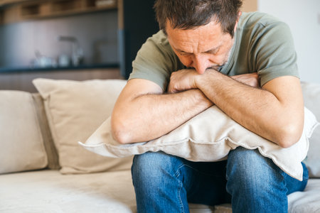 Desperate sad man sitting at sofa couch and hugging pillow, feeling miserable and depressed, selective focusの写真素材