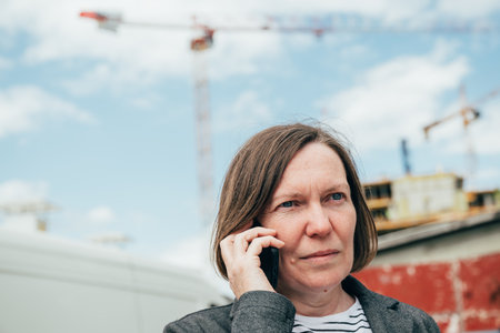 Portrait of elegant brunette businesswoman using mobile phone on construction site, selective focusの写真素材