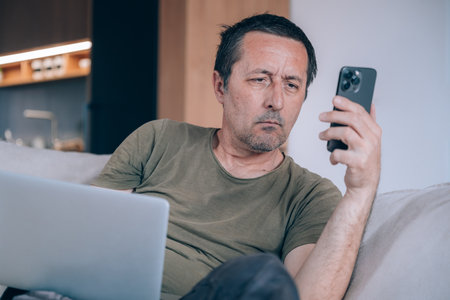 Telecommuter freelancer working online on a smartphone and laptop computer from his living room, selective focusの写真素材