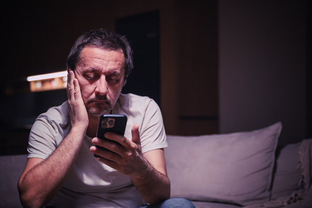 Tired exhausted man reading text message on mobile phone, selective focusの写真素材