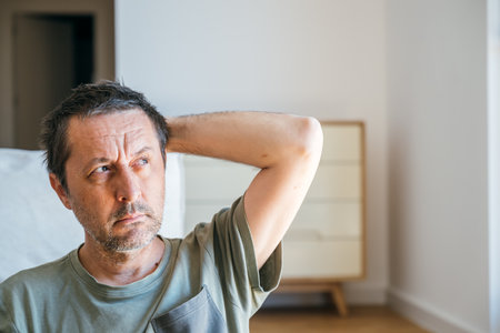 Portrait of pensive man sitting in living room in morning, thinking and looking out the window, selective focusの写真素材