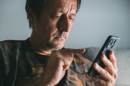Low key portrait of middle-aged man using mobile phone at home, selective focus