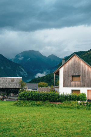 Contemporary home in the Alps with wooden facade, nestled in a peaceful valley with forested mountains and misty clouds. Selective focus.の写真素材