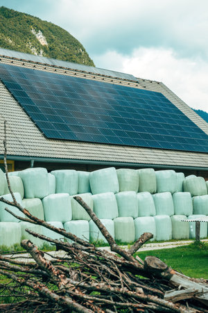 Large green silage bales neatly arranged along a rural farmyard, with mountains rising behind the barns. Selective focus.の写真素材