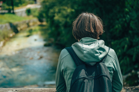 Female hiker with backpack admiring mountain river and traditional alpine village in Slovenia. Selective focus.の写真素材