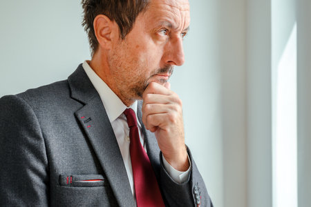 Concerned executive gazing out office window, reflecting on challenges and stress. Selective focus.