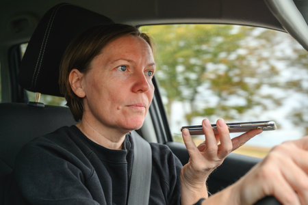 Irresponsible female driver talking on mobile phone while driving through countryside, holding phone in front of her face. Selective focus.の写真素材