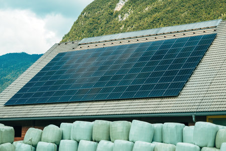 Solar panels on farm building roof with stacked hay bales wrapped in plastic sheets in front. Selective focus.の写真素材