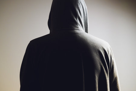 Rear view of man wearing light gray hooded shirt in low key light, unrecognizable person symbolizing anonymity and mystery. Selective focus.の写真素材