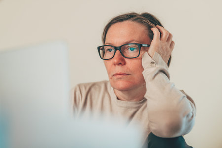 Mature adult woman in casual attire, stressed and frustrated while working on laptop computer at home. Selective focus.の写真素材