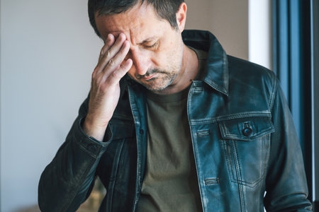 Confused adult man in leather jacket holding his head, concept of doubt, frustration, memory loss,...