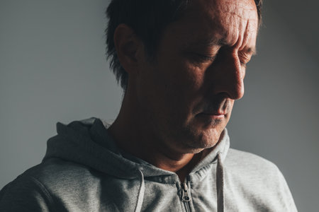 Low key portrait of mature man in casual clothing with eyes closed, expressing regret, sadness, and emotional reflection. Selective focus.の写真素材