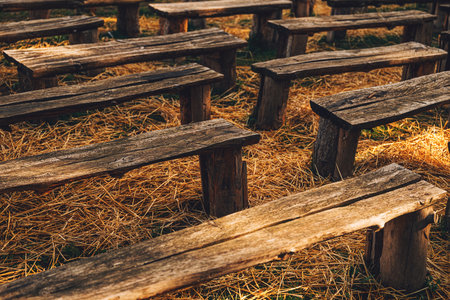 Rustic wooden benches arranged on dry straw outdoors, warm sunlight highlighting rough natural texture in a rural setting. Selective focus.の写真素材