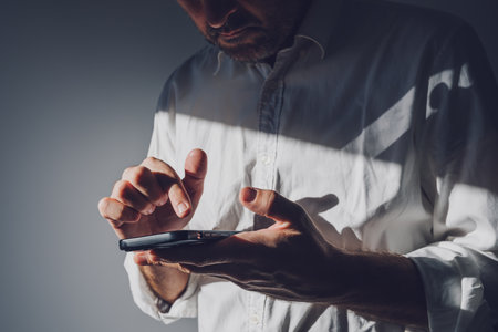 Closeup of businessman in white shirt typing text message on smartphone in office with dramatic...