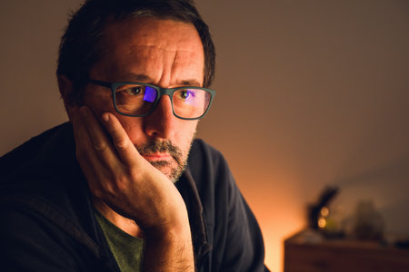 Portrait of mature man with eyeglasses in low key warm light, reflecting deep thought and overthinking concept, introspection, and mental fatigue. Selective focus.の写真素材