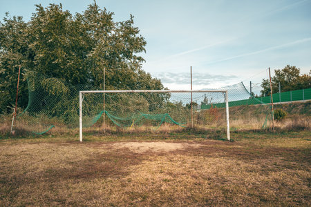 Old soccer goal on worn, uneven pitch with damaged grass and dusty ground, symbol of time and use. Selective focus.の写真素材