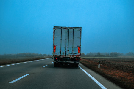Rear view of cargo truck traveling on rural highway in misty weather on a foggy morning under blue sky tones, selective focusの写真素材