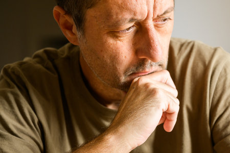 Indoor portrait of a pensive man resting his chin on his hand, thoughtful expression symbolizing...