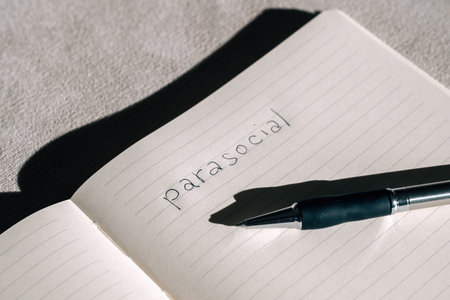 Handwritten word Parasocial on a blank notebook page with a pencil beside it, captured in harsh light with strong shadows for a dramatic, minimalist look. Selective focus.の写真素材