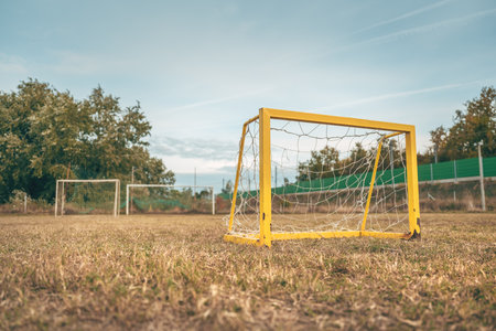 Yellow mini football goals standing on a weathered pitch, symbol of childhood play and fading sports...
