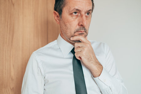 Thoughtful professional in formal attire resting hand on chin, contemplating strategy and business choices. Selective focus.の写真素材
