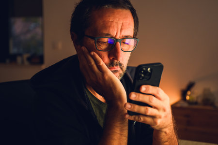 Evening solitude and digital focus â a man absorbed in his smartphone, surrounded by warm ambient light and quiet reflection. Selective focus.の写真素材