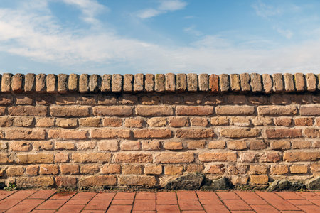 Old brick wall with terracotta coping and blue sky background, selective focus
