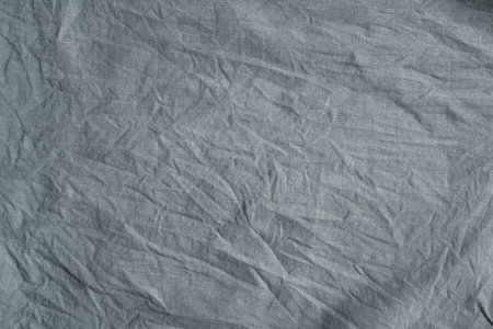 Close-up texture of heavily crumpled gray fabric with deep creases, fine weave, and soft shadows...