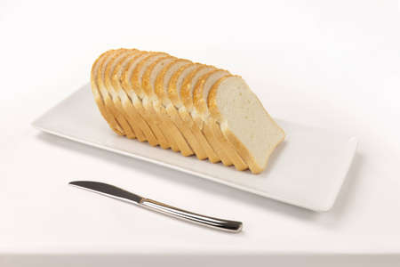 A sliced bread on a rectangular dish and a knife on a white tablecloth の写真素材