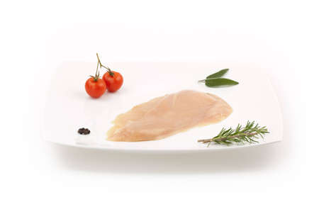 Raw chicken breast on white minimal dish with herbs, spice and small tomatoesの写真素材