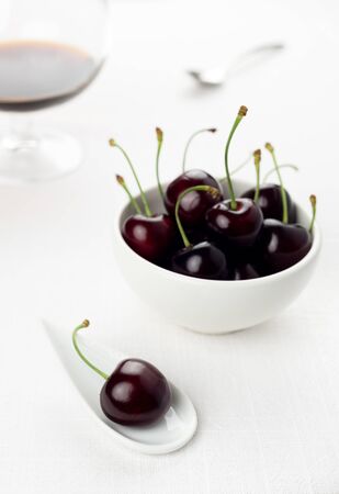 Single cherry on a white china spoon, a cherries group in a small round white bowl and a sherry glass with a spoon on backgroundの写真素材