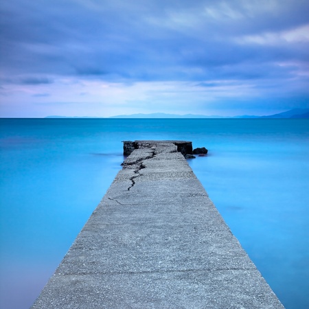 Broken concrete pier or jetty and rocks on a blue sea  Hills on background  Long exposure photography の写真素材