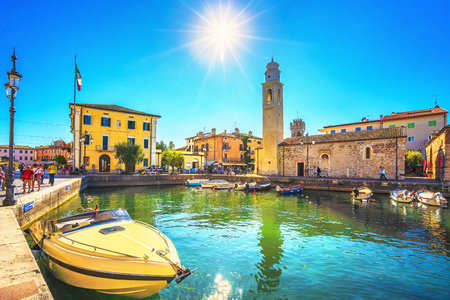LAZISE, VENETO / ITALY - SEPTEMBER 28, 2018: Boats in old town port of Lazise and tourists walking in the morning. The town is a popular holiday destination in Garda Lake district.のeditorial素材