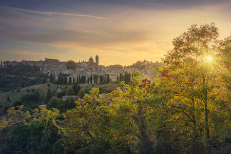 The skyline of Urbino city and the setting sun among the trees. Marche region, Italy, Europe.