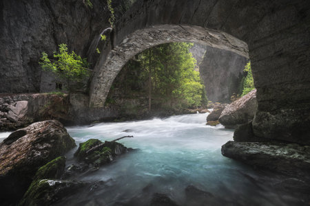 An old stone bridge over the stream in the Orrido of PrÃ© Saint Didier, a view in summer of this deep ravine in Aosta valley. Italy.の写真素材